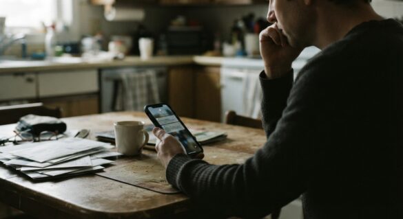 a person holding a phone with a disconnected service notice on the screen, looking concerned at a kitchen table